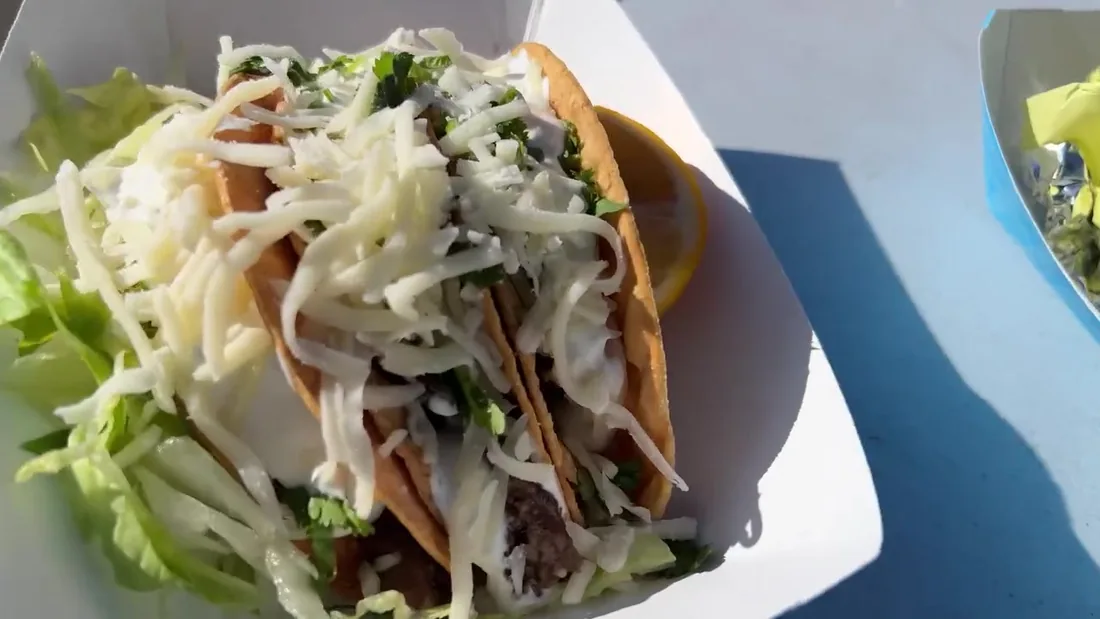 Tacos topped with shredded cabbage, cheese and cilantro in a paper tray