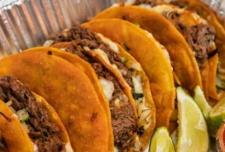 A tray of carne asada tacos with lime wedges