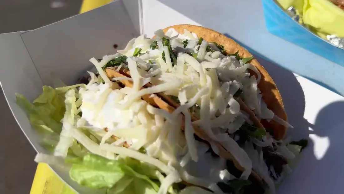 Street tacos in a paper boat topped with cheese, cabbage and cilantro