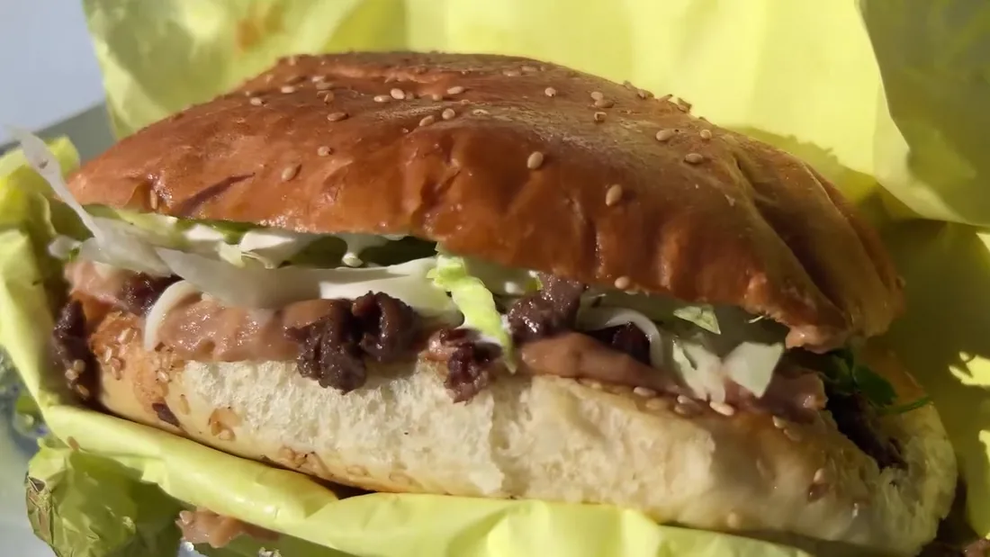 A torta on a toasted sesame roll filled with grilled meat, cabbage and crema